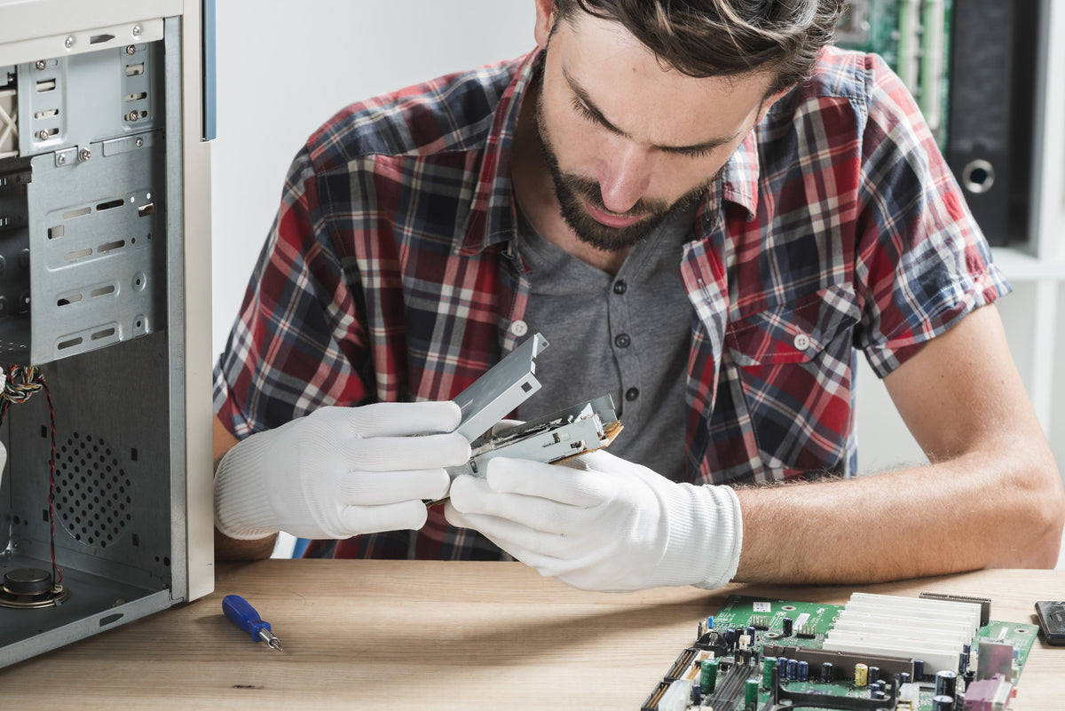 Technician in gloves examining a computer component at a refurbishment bench